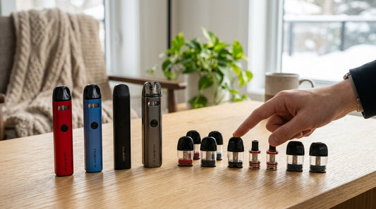 A hand selects from various Uwell Caliburn devices and pods arranged on a wooden table for performance comparison.