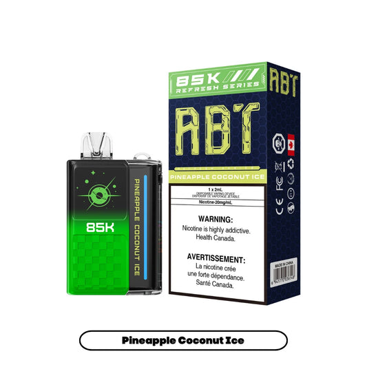 A green and black ABT 85K disposable vape device stands next to its matching product box, which features the flavor name Pineapple Coconut Ice and prominent health warning text in English and French against a dark blue honeycomb background.