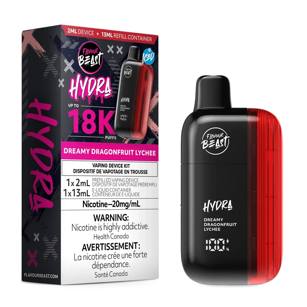 A Flavour Beast Hydra Dreamy Dragonfruit Lychee disposable vape device stands next to its black and pink retail box, which features a 13mL refill container, a 2mL device, and prominent 18K puff count branding against a plain white background.