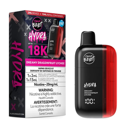 A Flavour Beast Hydra Dreamy Dragonfruit Lychee disposable vape device stands next to its black and pink retail box, which features a 13mL refill container, a 2mL device, and prominent 18K puff count branding against a plain white background.