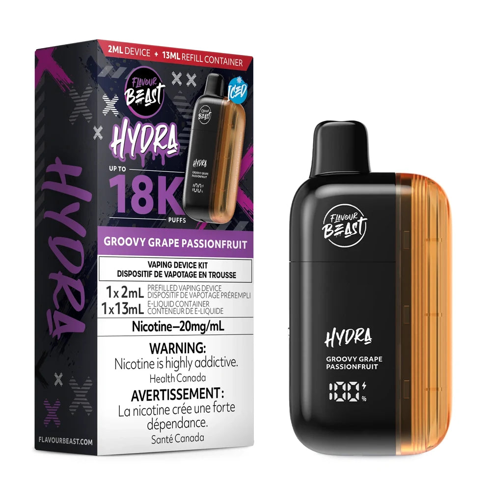 A Flavour Beast Hydra Groovy Grape Passionfruit disposable vape kit stands next to its black and purple retail box, which features a 20mg/mL nicotine warning and a 18,000 puff capacity label, against a plain black background.